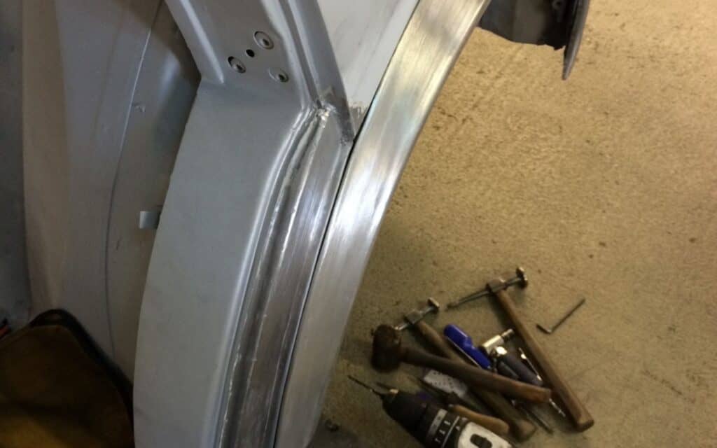 Classic car bodywork repair with tools and metalwork.