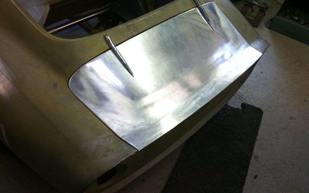 Custom metal car body panel being crafted in workshop.