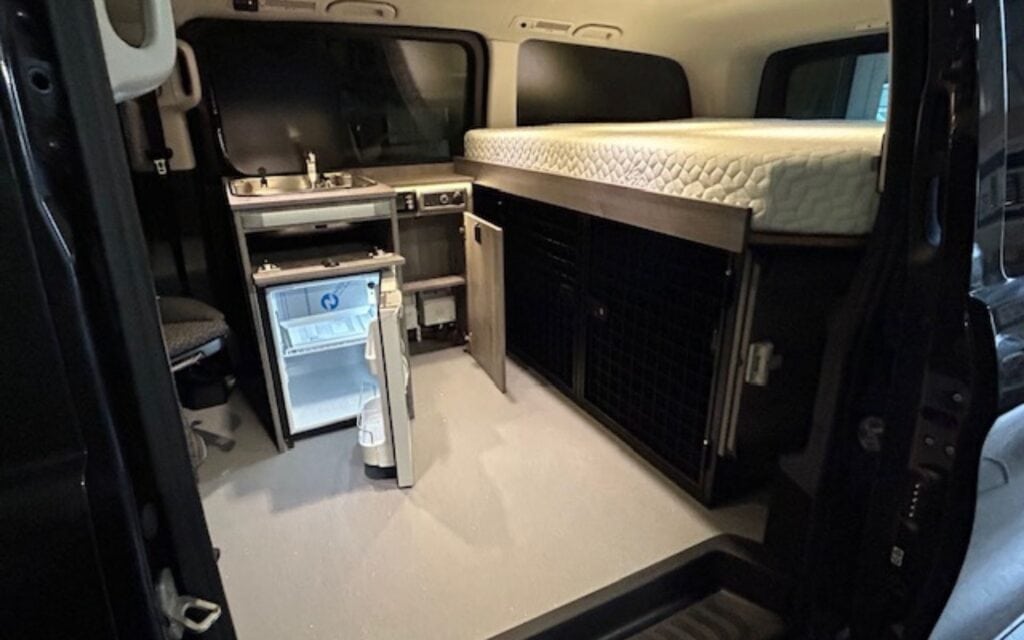 Interior view of a customized camper van featuring a sleeping platform, compact kitchen, and storage.