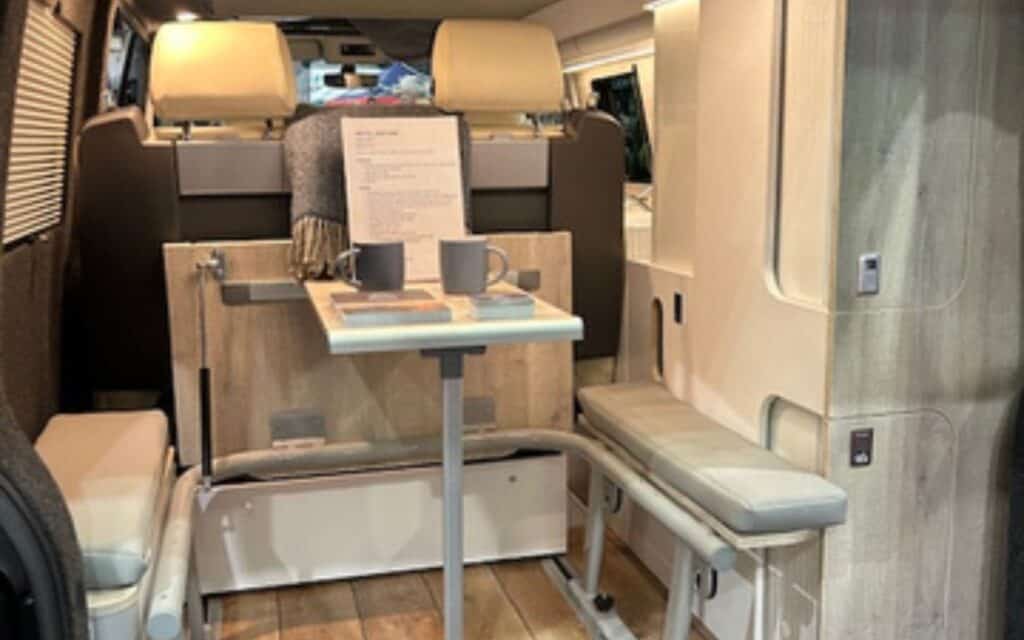 Interior view of a custom camper van with seating, table, and storage solutions.